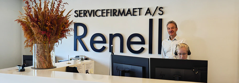 Receptionsområde hos Servicefirmaet Renell A/S med logo på væggen, tørrede blomster og personale bag skranken.