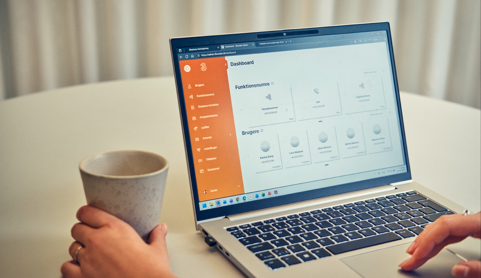 Hånd holder kaffekop ved bærbar computer, der viser et 3-dashboard med funktionsnumre og brugeroplysninger.