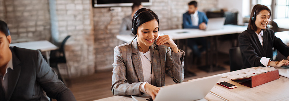 Kundeservicemedarbejdere med headsets arbejder ved computere i et moderne kontor med murstensvægge.