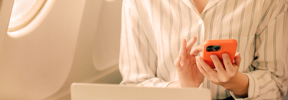 Person i stribet skjorte bruger orange mobiltelefon. Tekst: "Arbejd på rejsen - og i luften" med SAS WiFi-reklame.