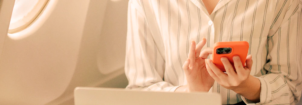 Person i stribet skjorte bruger orange mobiltelefon. Tekst: "Arbejd på rejsen - og i luften" med SAS WiFi-reklame.