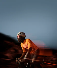 Fitness lifestyle "Cyklerytter i orange trøje og briller, hvid hjelm, sløret naturen i baggrunden"