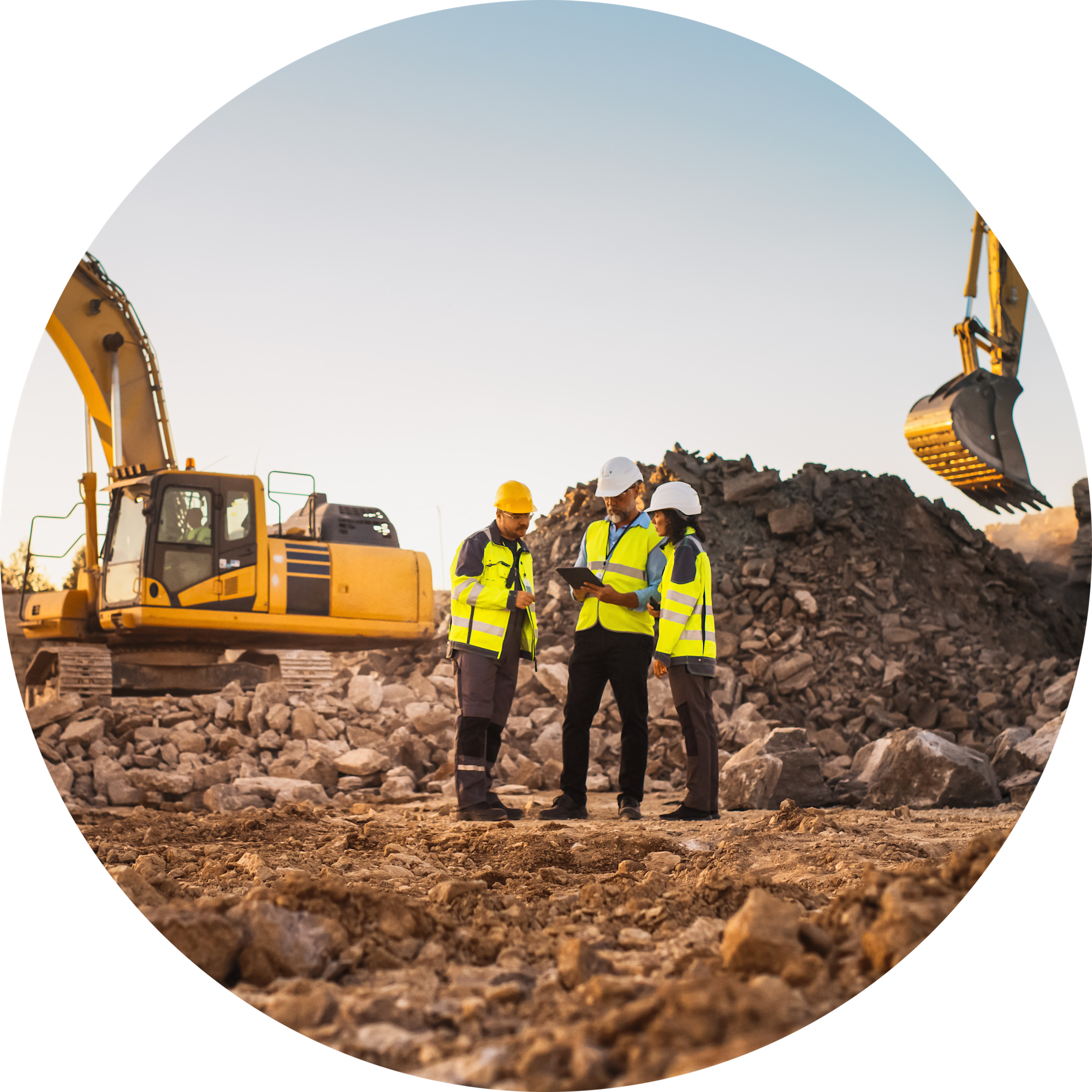 Tre personer i sikkerhedsveste og hjelme på byggeplads med gule gravemaskiner og bunker af sten ved solnedgang.