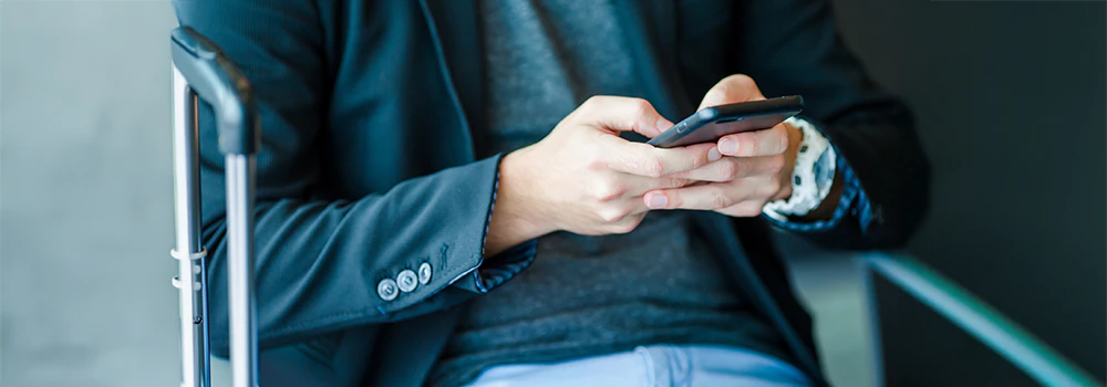 Mand der sidder med sin telefon og en kuffert