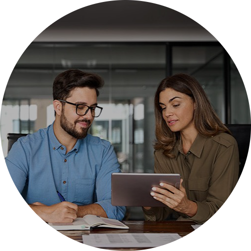 To personer i et kontormiljø ser sammen på en tablet, mens de samarbejder om et projekt ved et træbord.