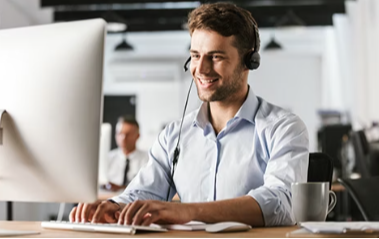 Smilende kundeservicemedarbejder med headset arbejder ved computer i et moderne kontormiljø.