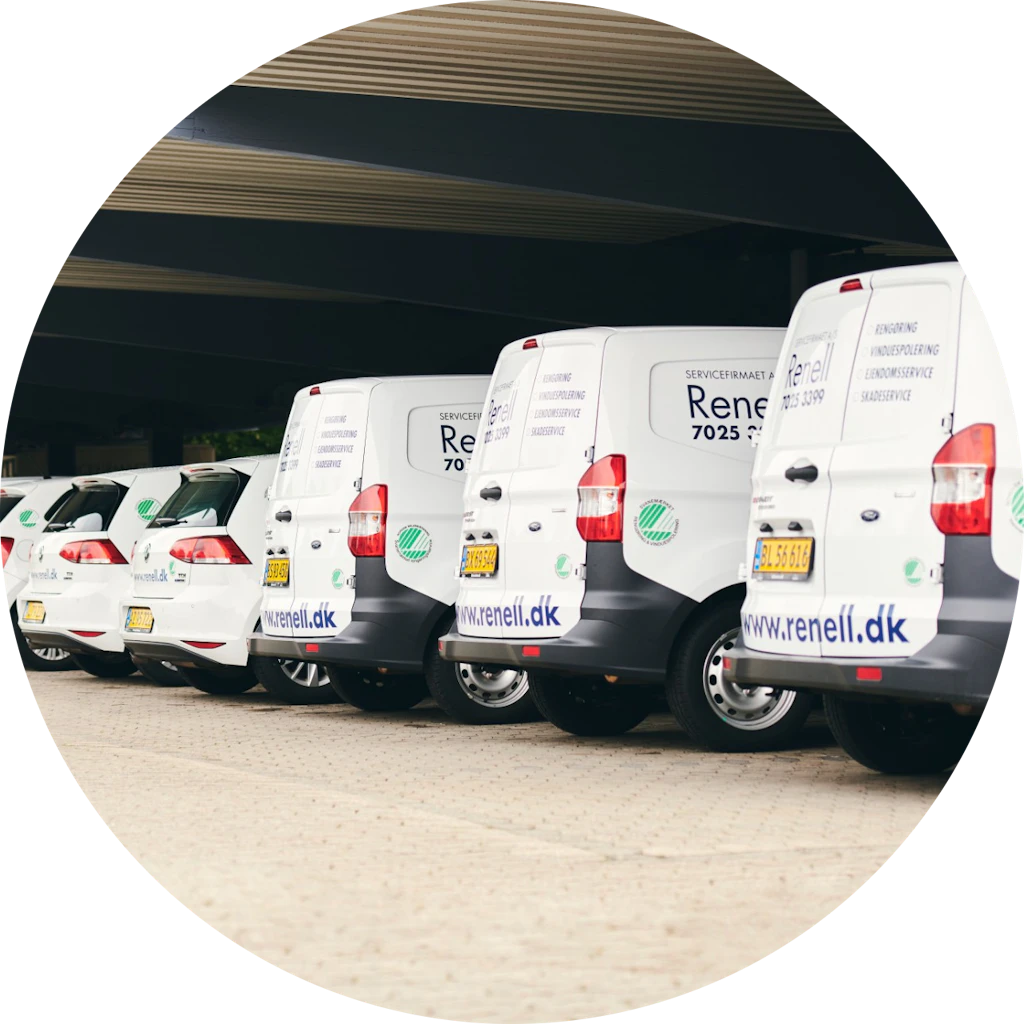 Række af hvide Renell servicebiler parkeret under et overdækket område med firmaets logo og hjemmeside synligt på bilerne.
