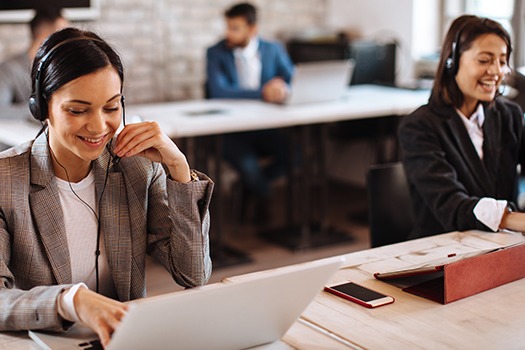 Personer med headsets arbejder ved computere i et moderne kundeservicecenter med murstensvægge.